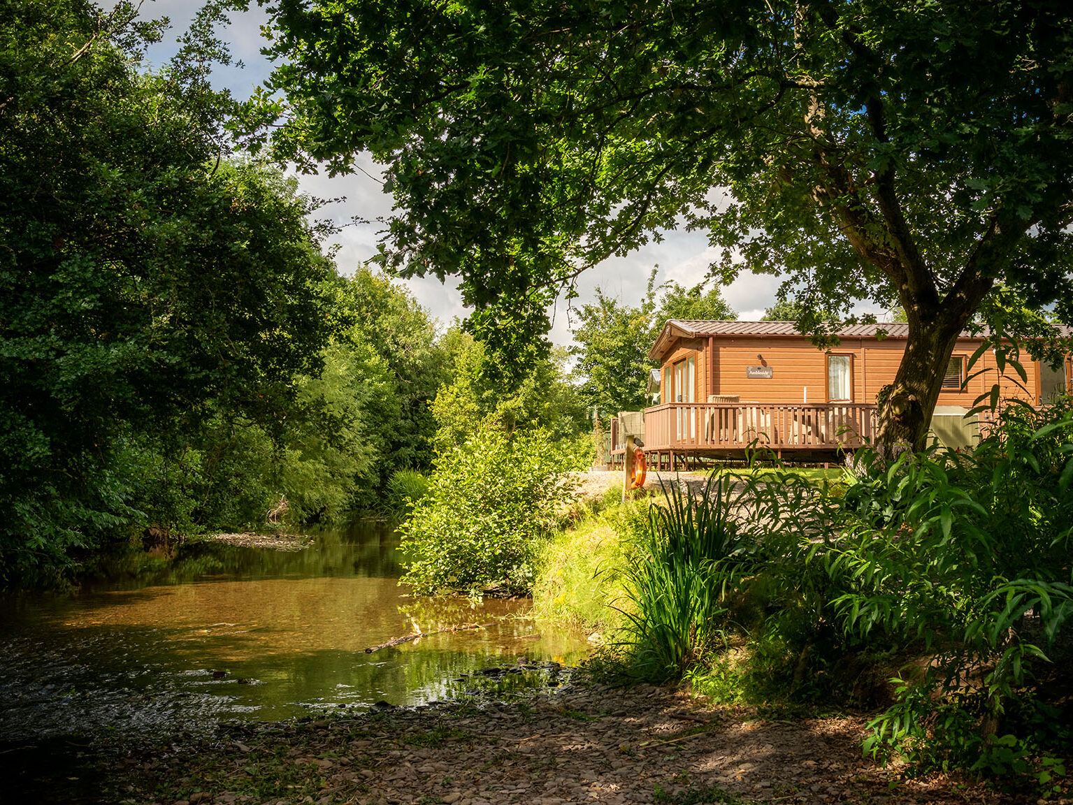 The River Arrow flowing through wooded banks at Arrow Bank Country Holiday Park, shallow rocky bed and overhanging branches visible
