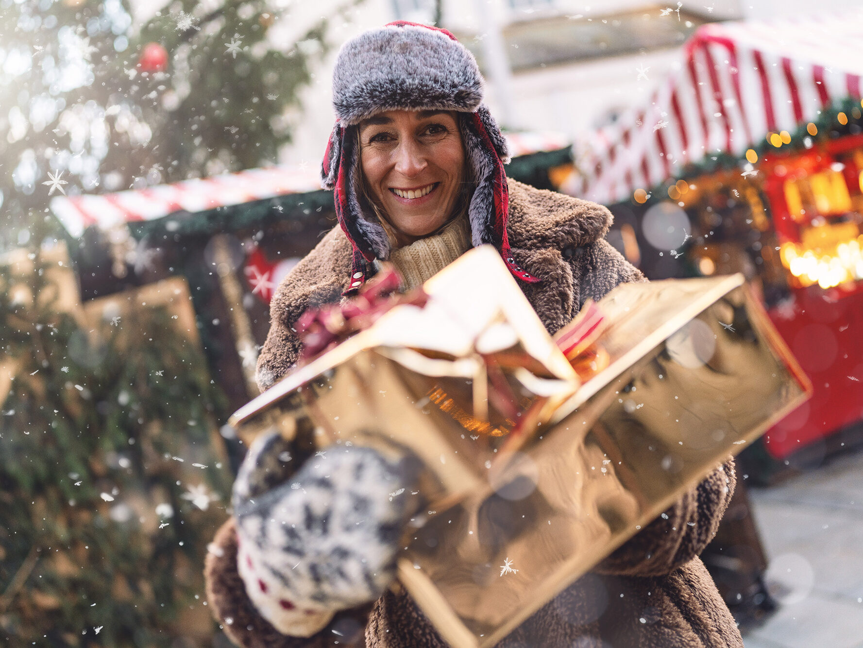 Woman holding Christmas presents at a festive market stall in Shropshire, surrounded by snow and twinkling lights.