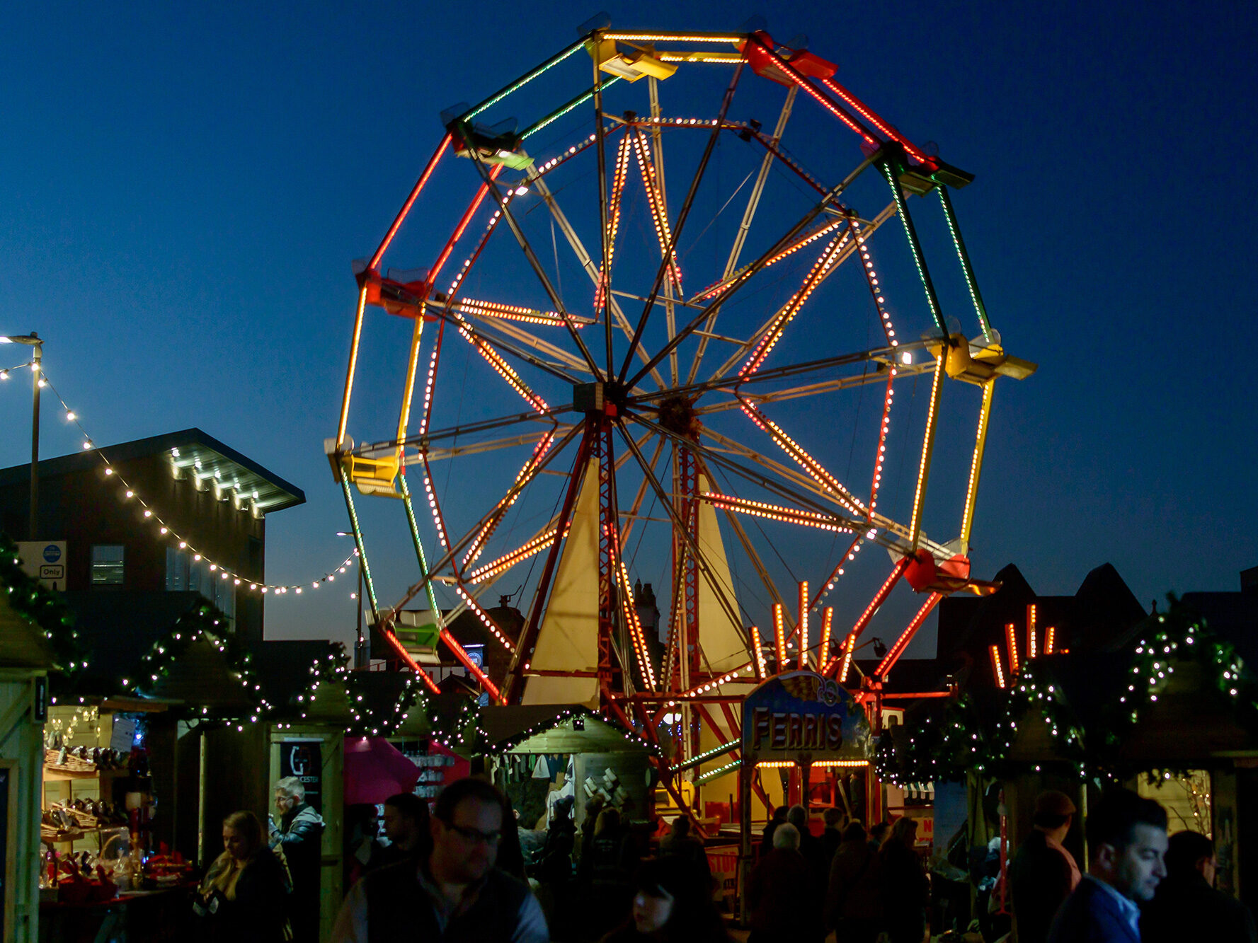 Ferris wheel lit up at night at Gloucester Quays Christmas Market, surrounded by festive stalls and twinkling lights.